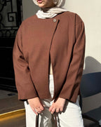 Person wearing a brown jacket and white pants standing outdoors.