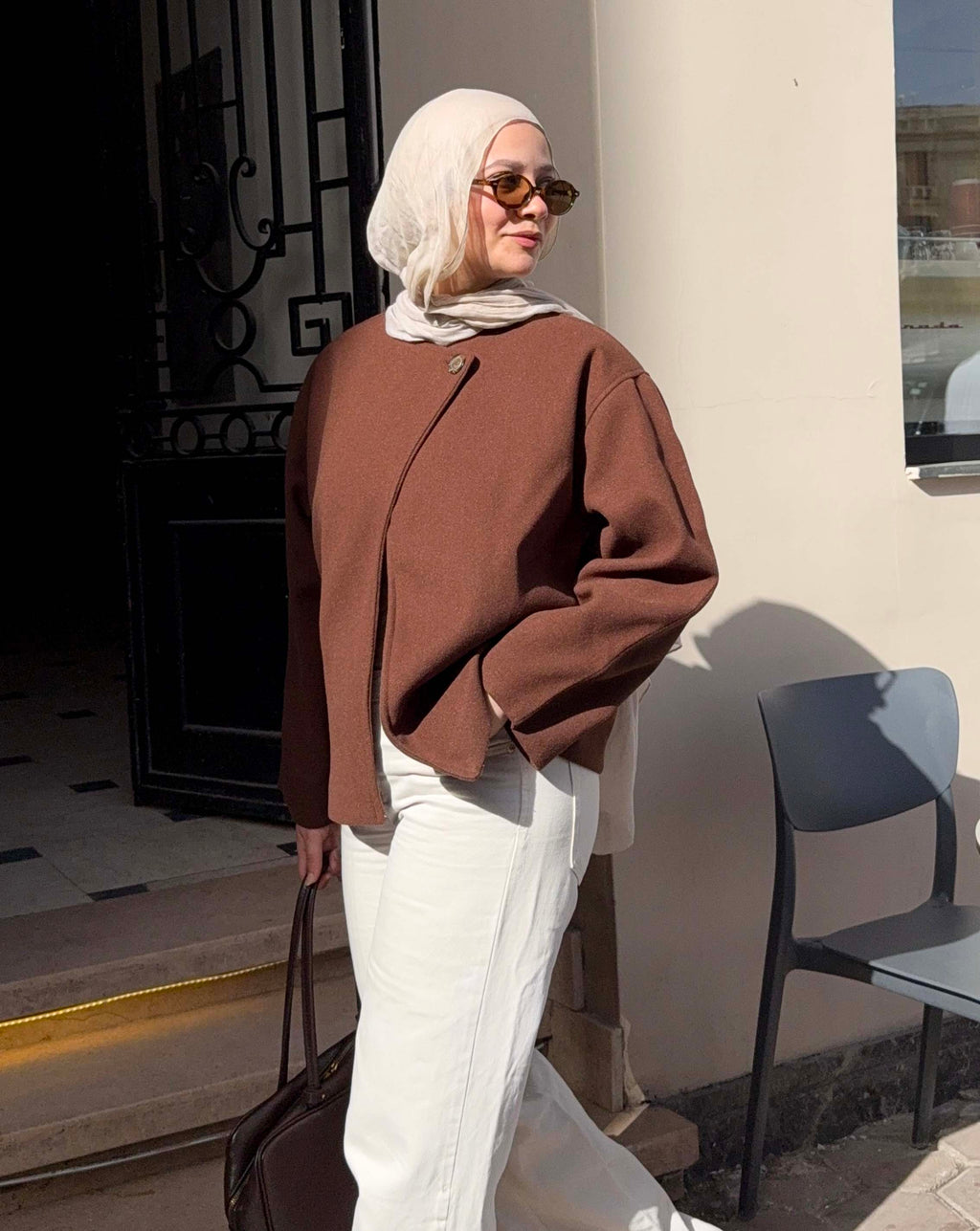 Woman wearing a brown jacket and white hijab standing outdoors.